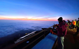 Climbers watching sunrise above clouds on Mt. Fuji summit during climbing tour.