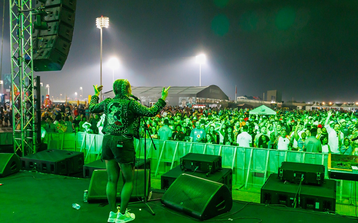 Performer on stage at Emirates Dubai 7s with a cheering crowd at night.