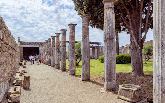 Visitors exploring ancient columns at Pompeii ruins, Italy.