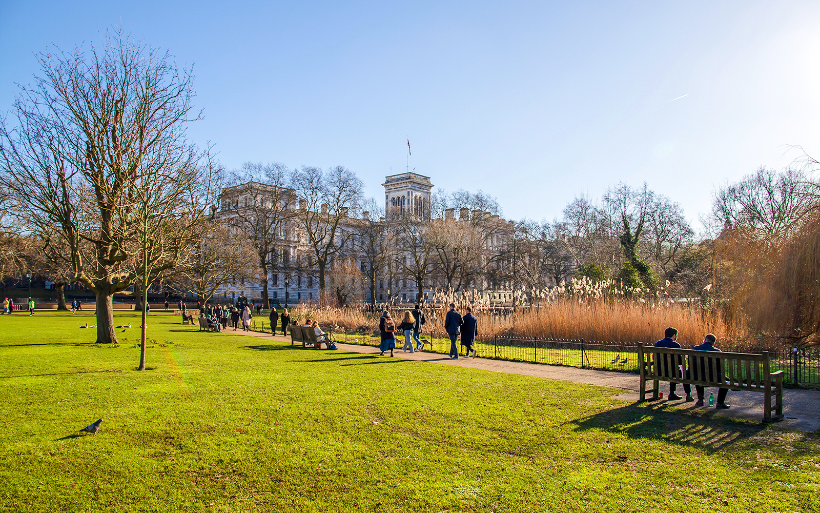 People walking and sitting in St James's Park, London, with a historic building in the background.