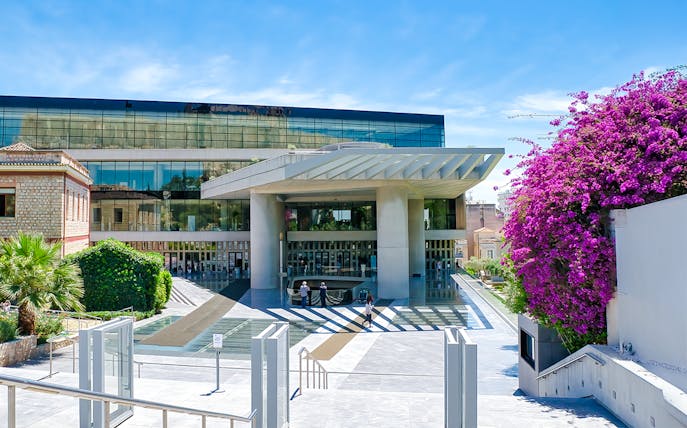 Acropolis Museum entrance with modern architecture and vibrant flowers, Athens, Greece.