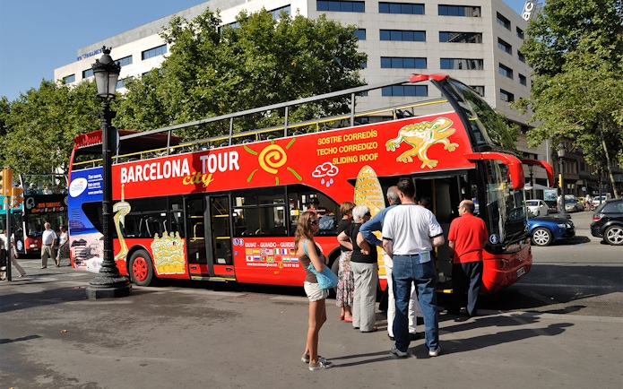 Barcelona hop-on hop-off bus with tourists boarding near city landmarks.