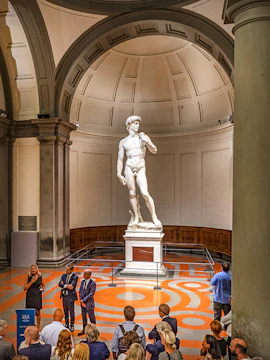 Statue of David in Florence's Accademia Gallery with visitors gathered around.