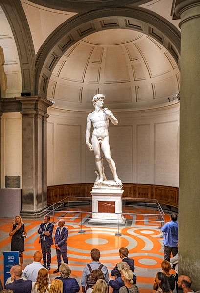 Statue of David in Florence's Accademia Gallery with visitors gathered around.