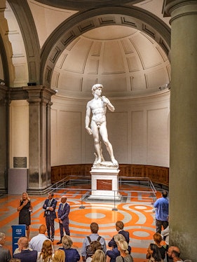 Statue of David in Florence's Accademia Gallery with visitors gathered around.