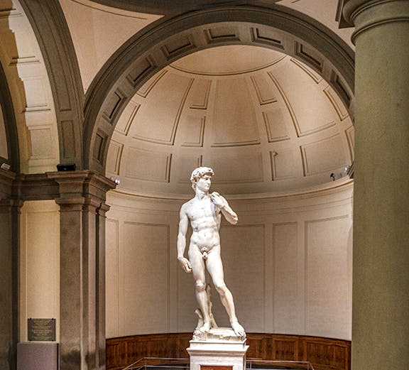 Statue of David in Florence's Accademia Gallery with visitors gathered around.