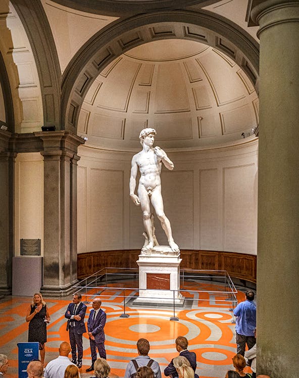 Statue of David in Florence's Accademia Gallery with visitors gathered around.