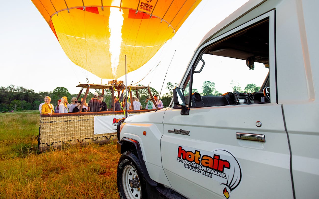 Hot air balloon preparing for flight with passengers in Gold Coast, near a branded vehicle.