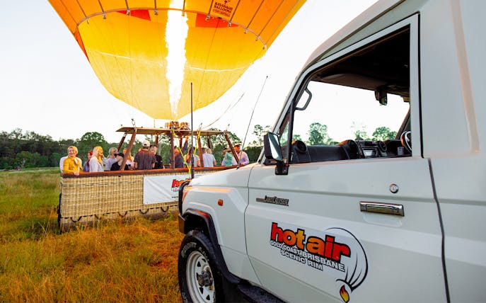 Hot air balloon preparing for flight with passengers in Gold Coast, near a branded vehicle.