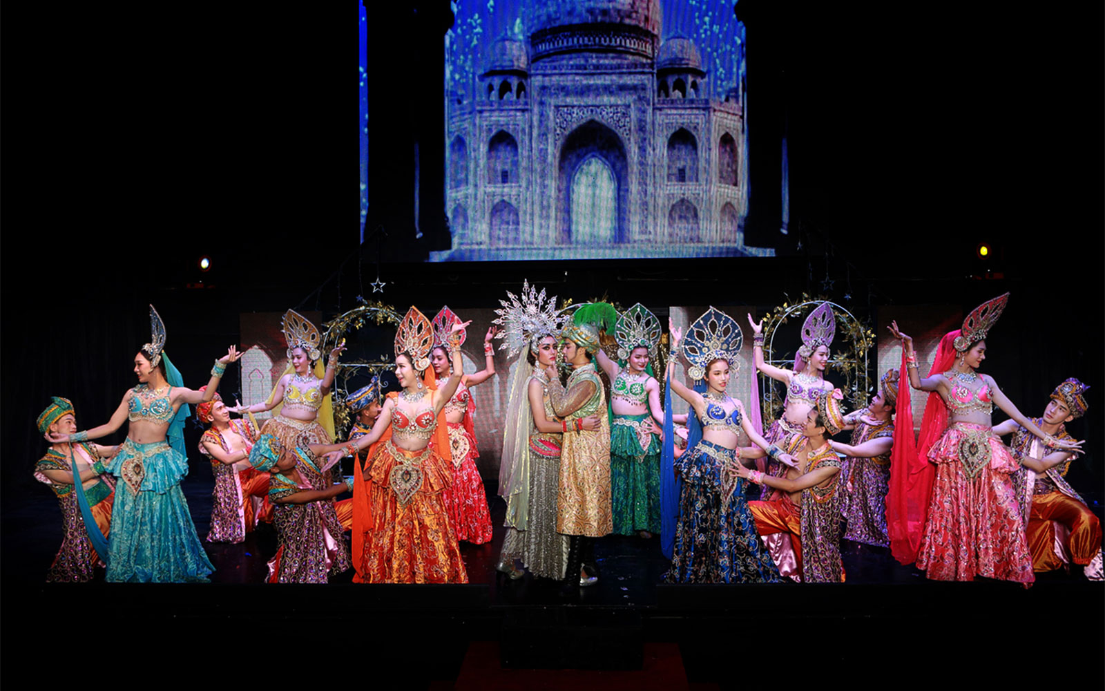 Performers in colorful costumes on stage at Siam Dragon Cabaret Show, with a backdrop of an ornate building.