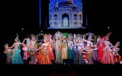 Performers in colorful costumes on stage at Siam Dragon Cabaret Show, with a backdrop of an ornate building.