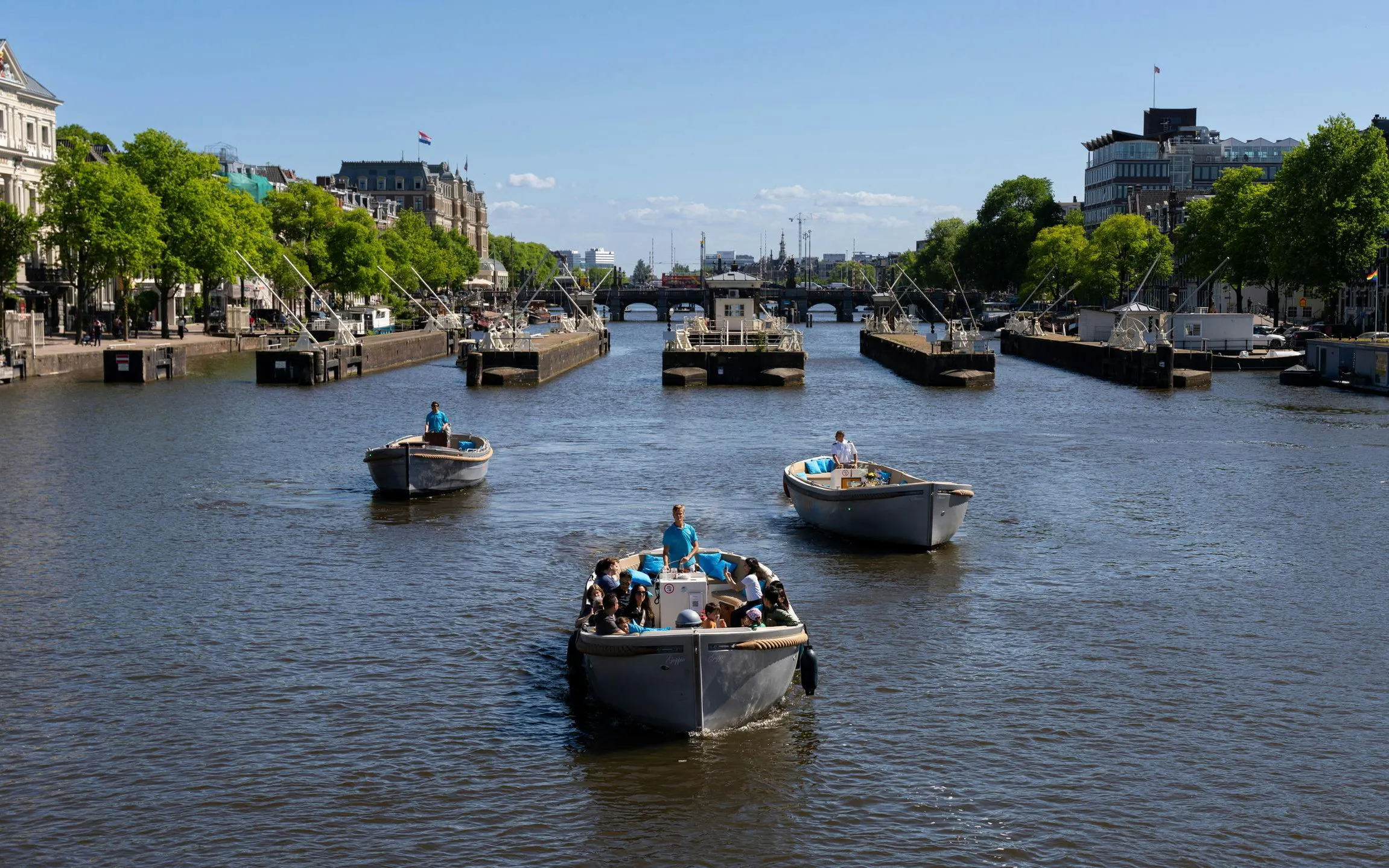 Open electric boat cruising Amsterdam canal near Central Station.