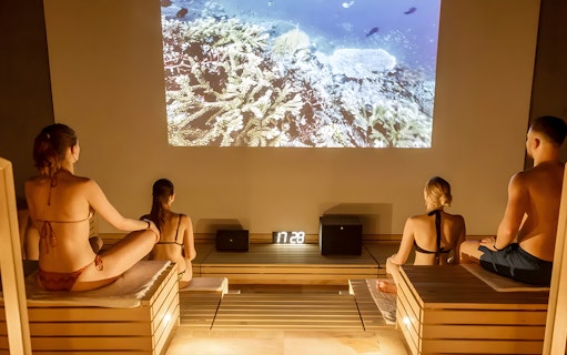 Visitors relaxing in a sauna at Therme Bucuresti Spa, watching an underwater video.