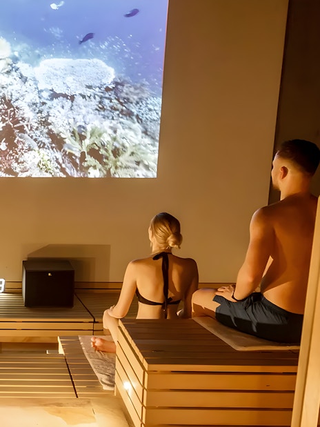 Visitors relaxing in a sauna at Therme Bucuresti Spa, watching an underwater video.