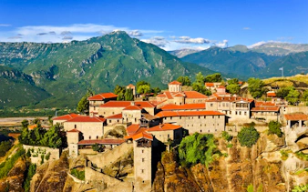 Great Meteoron Monastery on rocky cliffs with mountain backdrop in Greece.