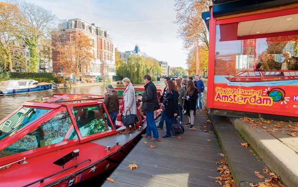 People boarding City Sightseeing hop on hop off boat in Amsterdam canal.
