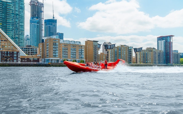 Thames speed boat with passengers cruising past London riverside buildings.