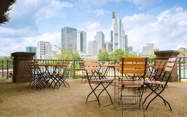 Cafe tables and chairs overlooking Frankfurt cityscape with skyscrapers.