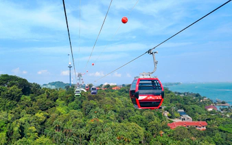 Tourists riding Singapore Cable Car over lush greenery and coastline.
