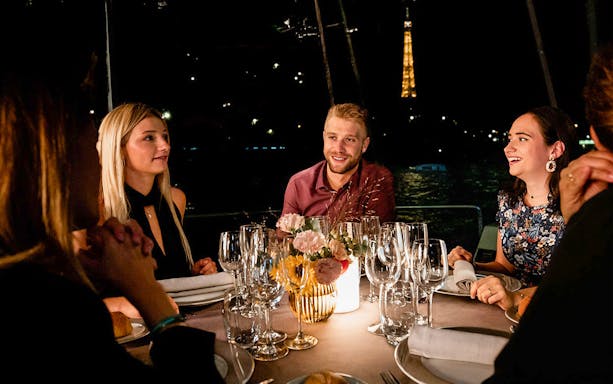 Guests dining on a Seine River cruise with Eiffel Tower view.