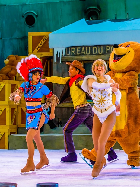 Performers in colorful costumes ice skating at Astérix Park show.