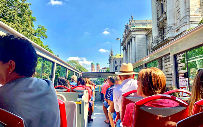 Tourists on an open-top Citysightseeing Munich bus with Frauenkirche in view.