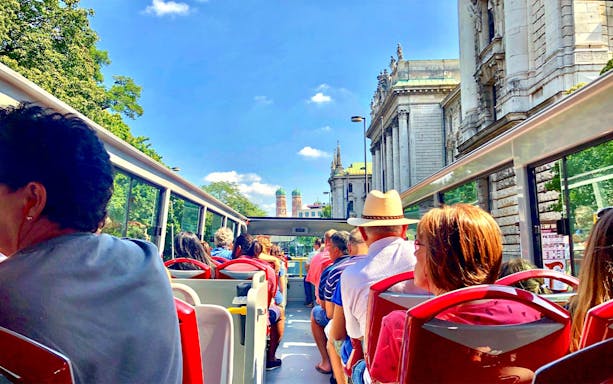 Tourists on an open-top Citysightseeing Munich bus with Frauenkirche in view.