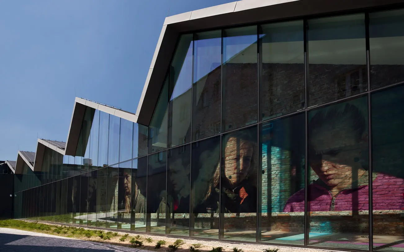 Glass facade of Krakow museum reflecting portraits, part of the Krakow Museum Pass tour.