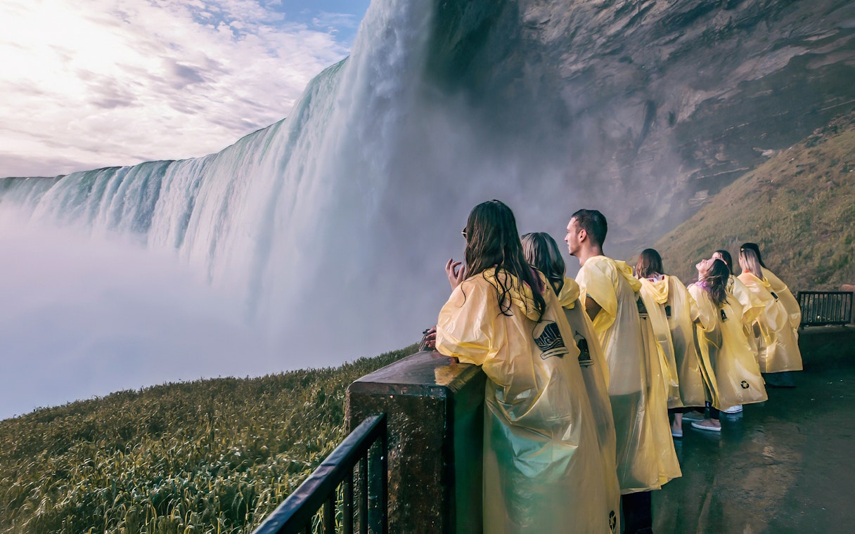Visitors in yellow ponchos view Niagara Falls from a platform on a day tour from Toronto.