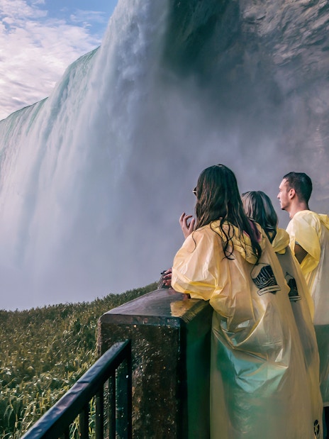 Visitors in yellow ponchos view Niagara Falls from a platform on a day tour from Toronto.
