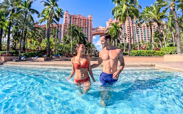 Couple enjoying pool at Atlantis Aquaventure, Nassau, Bahamas with resort in background.