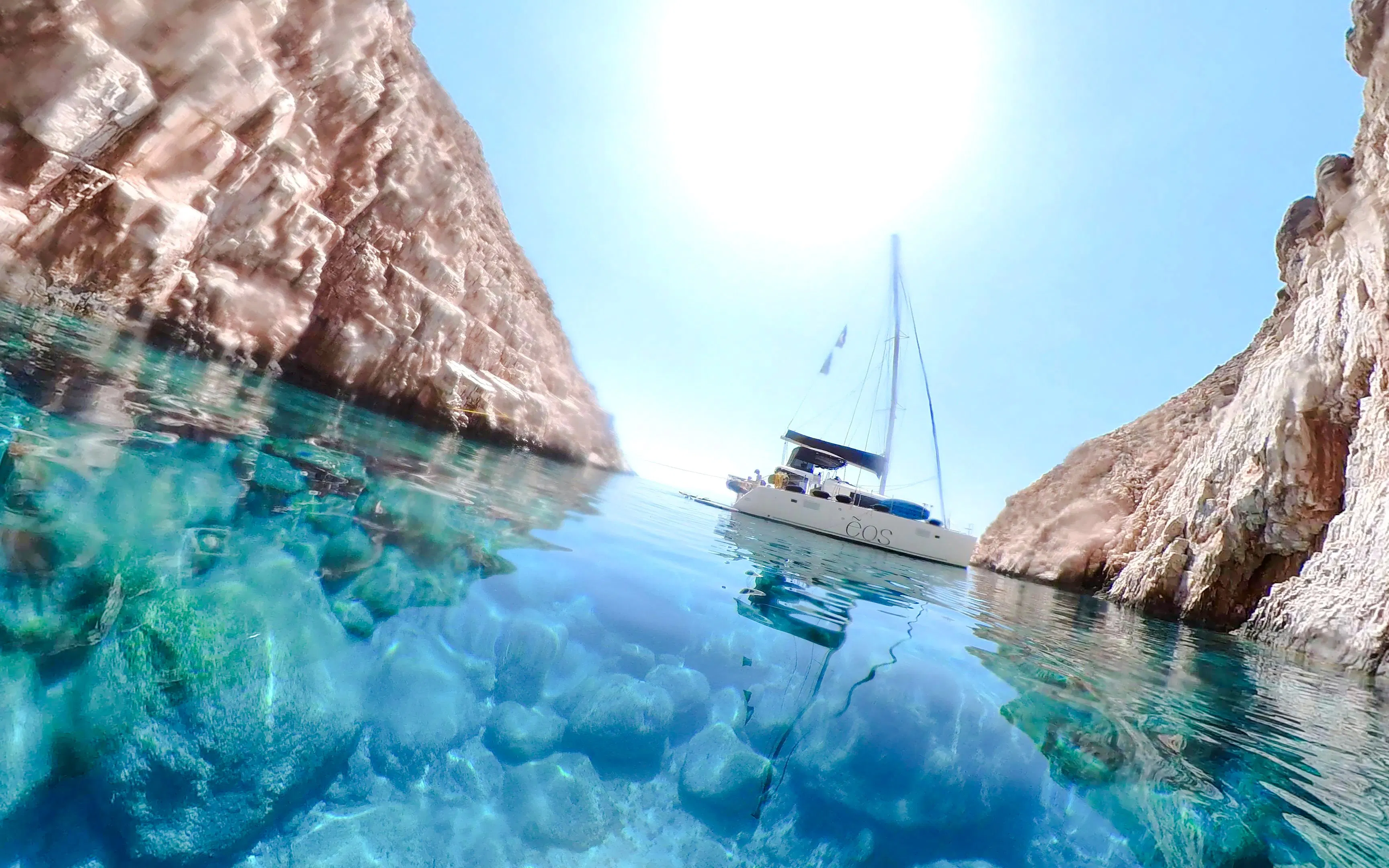 Catamaran sailing between rocky cliffs in Heraklion's clear waters.