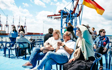 Guests relaxing on deck during 1-Hour Harbor Sightseeing Cruise with Hafen, cranes in background.
