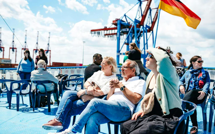Guests relaxing on deck during 1-Hour Harbor Sightseeing Cruise with Hafen, cranes in background.