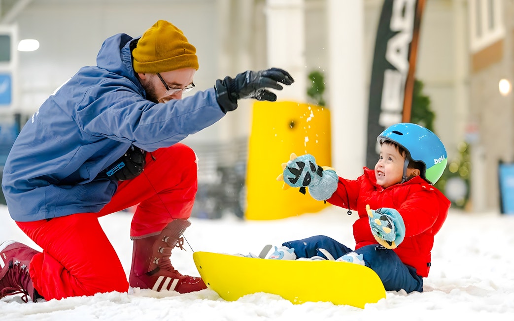 Child sledding indoors at American Dream's Big Snow, guided by an adult in winter gear.