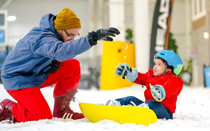 Child sledding indoors at American Dream's Big Snow, guided by an adult in winter gear.