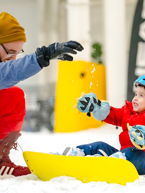 Child sledding indoors at American Dream's Big Snow, guided by an adult in winter gear.