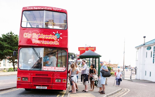Bournemouth sightseeing bus with tourists boarding at a stop near the beach.