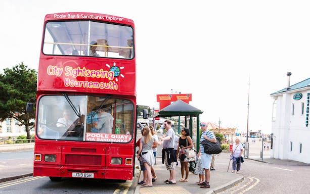 Bournemouth sightseeing bus with tourists boarding at a stop near the beach.