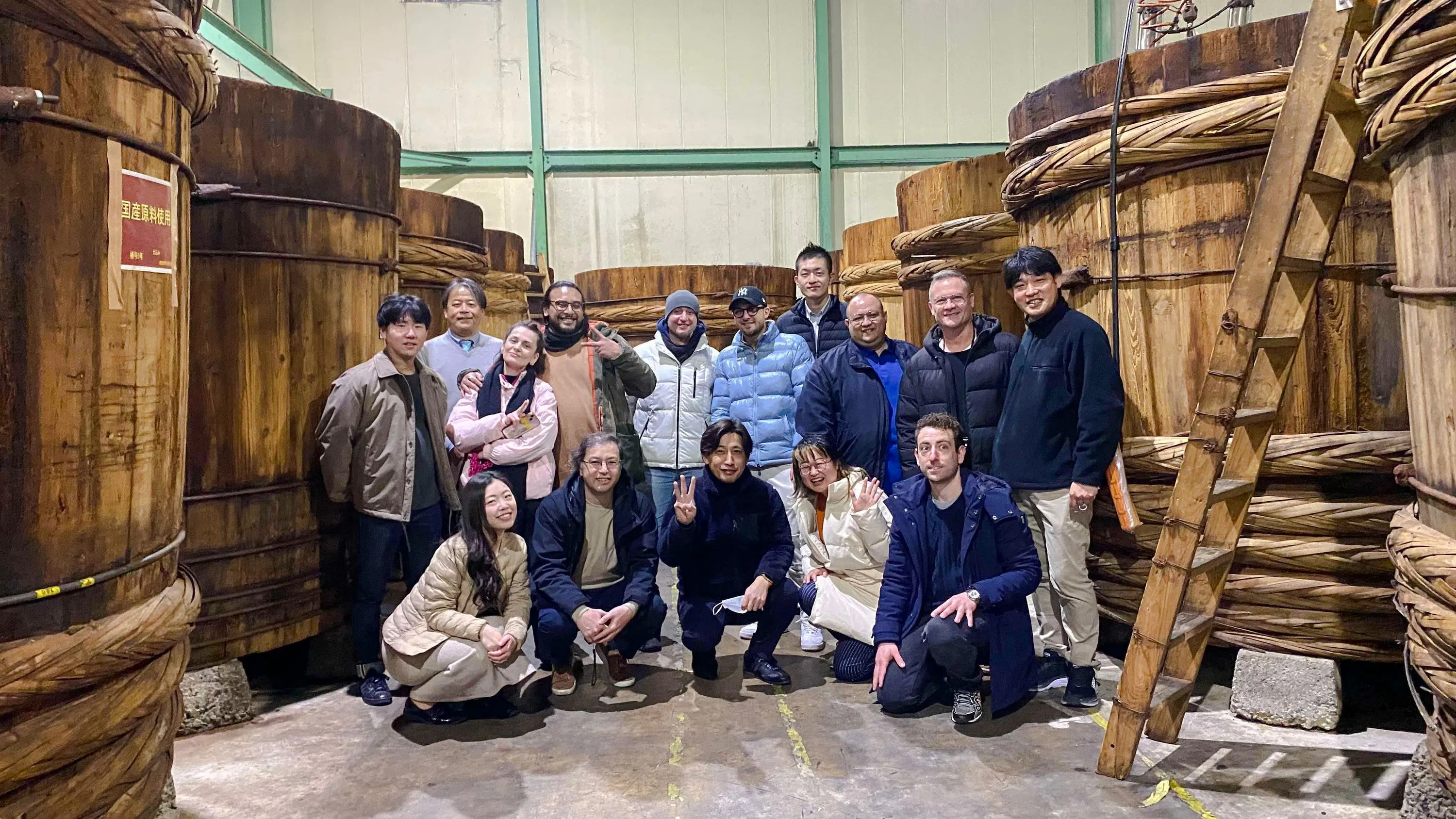 Group of people on a Sato Jozo Miso Brewery tour in Ama, Aichi, standing by large wooden barrels.