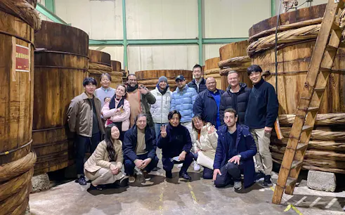 Group of people on a Sato Jozo Miso Brewery tour in Ama, Aichi, standing by large wooden barrels.