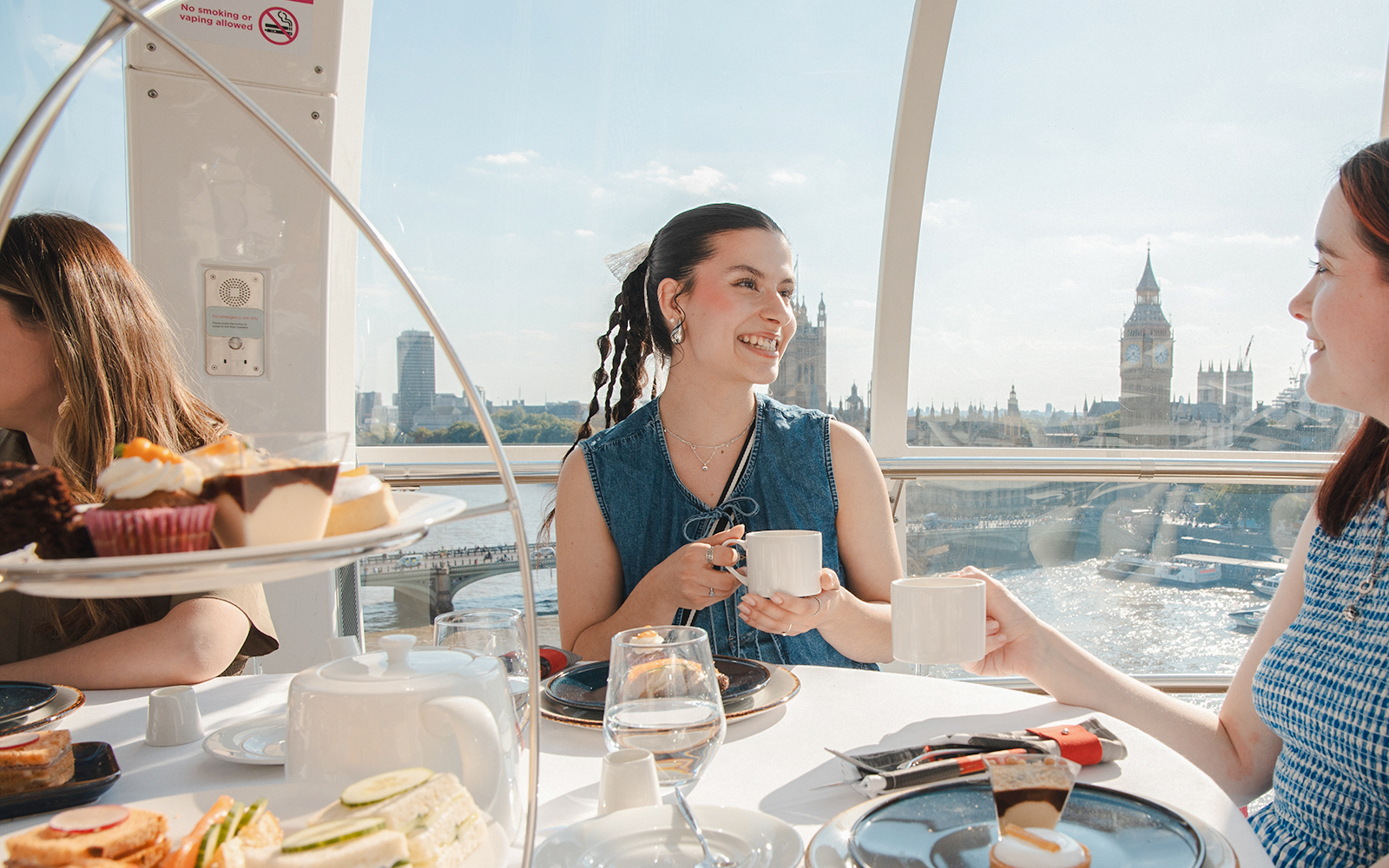 London Eye capsule with people enjoying afternoon tea, view of Big Ben and River Thames.