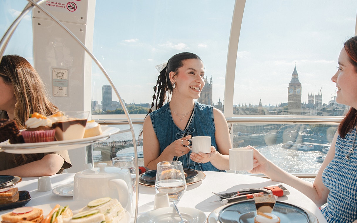 London Eye capsule with people enjoying afternoon tea, view of Big Ben and River Thames.