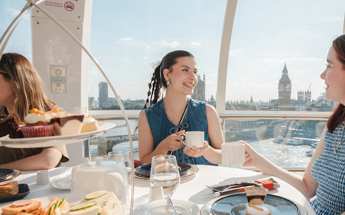 London Eye capsule with people enjoying afternoon tea, view of Big Ben and River Thames.