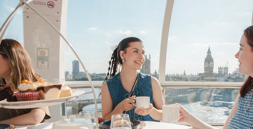 London Eye capsule with people enjoying afternoon tea, view of Big Ben and River Thames.