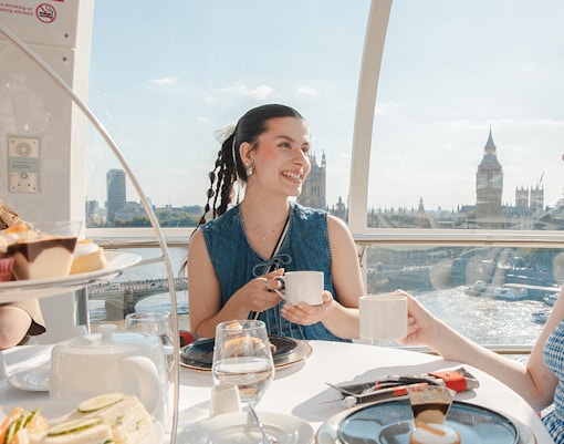London Eye capsule with people enjoying afternoon tea, view of Big Ben and River Thames.