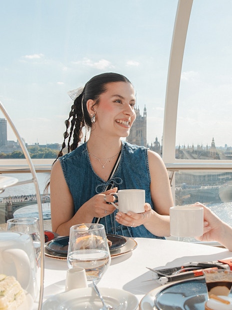 London Eye capsule with people enjoying afternoon tea, view of Big Ben and River Thames.