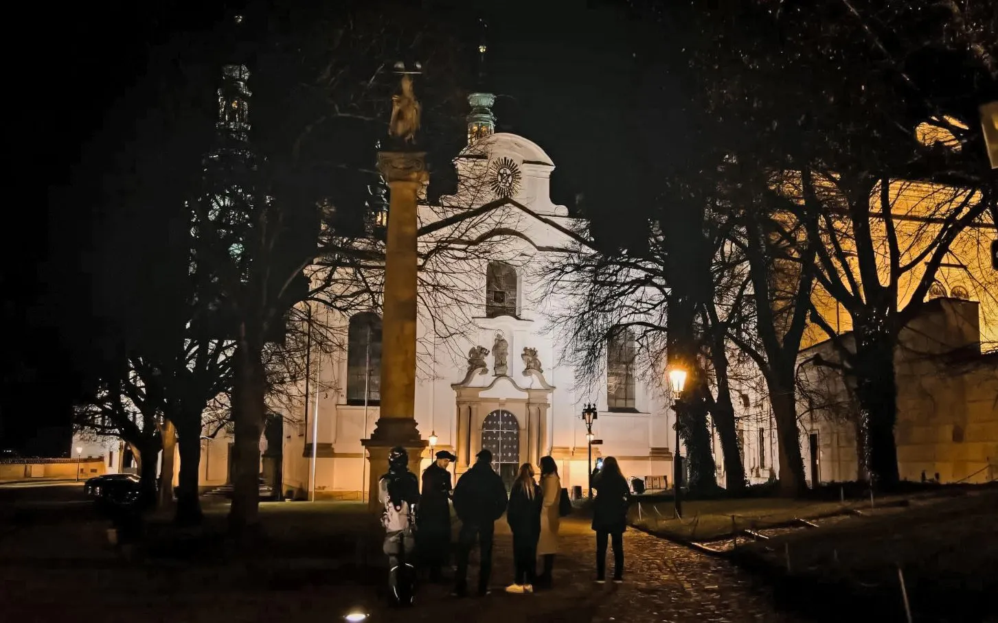 Night tour group at Prague Castle, standing near a lit historical building.
