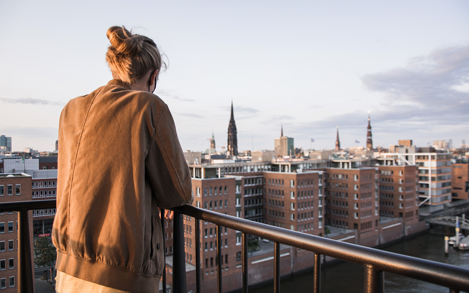Eine Frau steht auf einem Balkon und überblickt den Fluss und Hamburg