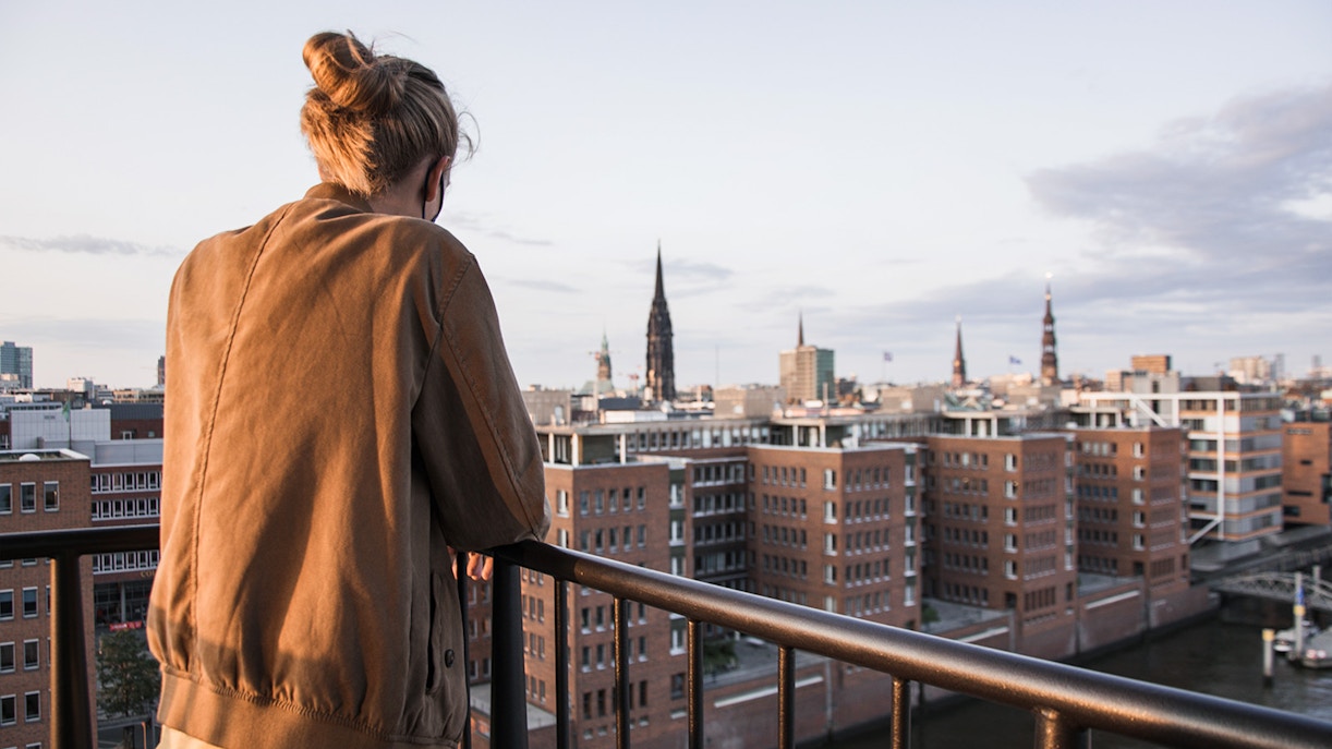 Eine Frau steht auf einem Balkon und überblickt den Fluss und Hamburg